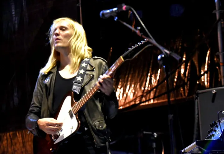 Guitarrista de pelo rubio actuando con una guitarra blanca
